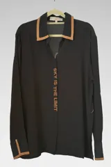 Camisa negra de manga larga con cuello clásico y puños con ribete color camel. Estampado vertical con la frase "Sky is the limit".
