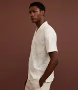 Camisa de manga corta color crema con bordado floral texturizado, cuello solapa y abotonadura frontal.