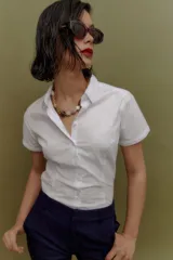 Camisa blanca de manga corta, con cuello camisero y botones frontales. Presenta un corte entallado al cuerpo.