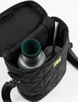 Bolso matero cilíndrico negro con diseño matelaseado, correa larga regulable y bolsillo trasero con cierre. Interior con velcro para sujetar el termo o mate.
