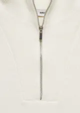 Chaleco de punto color crudo, con cuello polo y cierre de cremallera metálica. Tiene diseño sin mangas y ribete a rayas en el bajo.