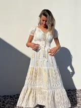 Vestido largo blanco con estampado dorado, escote en V con cordones y mangas cortas abullonadas.