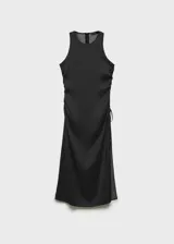 Vestido midi negro con estampado de lunares blancos, de tejido fluido y corte entallado. Presenta tirantes anchos, fruncido lateral con lazo, escote redondo y cierre de cremallera invisible en la parte posterior.