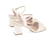 Sandalias de cuero color crema, con punta cuadrada, tira ancha sobre los dedos y pulsera al tobillo con hebilla. El tacón es cuadrado y mide 8 cm.