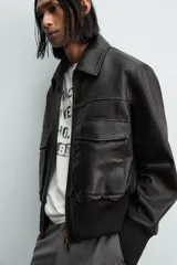 Cazadora estilo bomber cropped fit de piel negra, con cuello solapa, cierre frontal de cremallera, bolsillos frontales de plastrón con solapa y puños y bajo de rib elástico ancho.