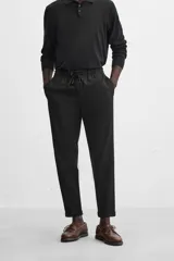 Pantalón negro de corte cropped, con cintura elástica ajustable con cordón, bolsillos laterales y traseros de vivo. El bajo tiene terminación con vuelta.