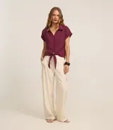 Blusa color borgoña de viscosa texturizada, con cuello, abotonada al frente, mangas cortas con dobladillo y lazo en la cintura.