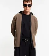 Cardigan de punto color marrón topo, con capucha negra contrastante y cierre frontal de cremallera negra. Presenta bolsillos laterales.