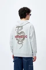 Canguro marrón con capucha, bolsillo frontal y puños ajustados. Estampa frontal con la palabra 'Dramatic' y gráfico en la espalda con tipografía bold y serpiente ilustrada.