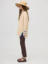 Sweater color crema con tejido en ochos, cuello redondo, puños acanalados con doble raya azul y tajos a los costados.