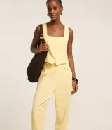 Pantalón zanahoria de cintura alta color amarillo pastel, confeccionado en viscolino con 15% de lino, con trabillas en la cintura, solapas con botón abajo de la cintura, pliegues y cierre tradicional.