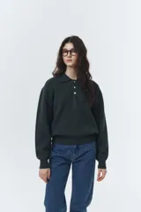 Sweater de punto color gris oscuro, con cuello tipo polo y tres botones blancos. Presenta un calce ligeramente holgado y puños y bajo acanalados.