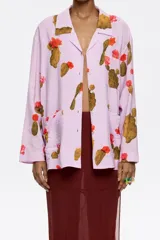 Camisa de viscosa color lila con estampado de cactus y flores rojas, corte recto, cuello con solapas, manga larga recta, cierre frontal con botones y bolsillos de plastrón.
