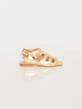 Sandalia de cuero vacuno color dorado, con tiras en capellada y hebillas metálicas ajustables.