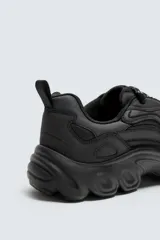 Zapatillas deportivas color crema con cordones, suela gruesa con diseño irregular y detalles en gris.