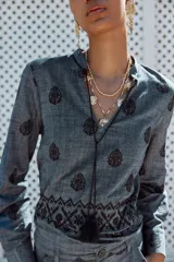 Blusa azul con bordados negros, cuello redondo con escote en pico y cordones ajustables terminados en borlas.