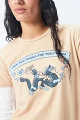Remera color beige de manga corta con cuello redondo y estampado con ilustración gráfica al frente y frase retro.