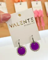 Aros colgantes con aro de acero plateado y dije circular color violeta con borde de strass plateado.