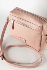 Bandolera color nude de símil cuero con acceso con cierre y herrajes plateados. Tiene un bolsillo interno con cierre, dos bolsillos externos abiertos y un bolsillo externo con cierre. La correa es regulable y el interior es de tela de algodón y poliéster.