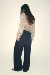 Camisa estampada con motivos paisley en tonos beige, rosa, lila y amarillo. Tiene cuello redondo con lazos, mangas largas abullonadas con puños elásticos y volantes en el delantero.
