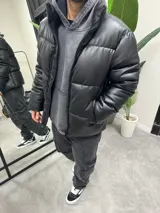 Campera puffer negra de símil cuero, con cuello alto y cierre frontal con cremallera.