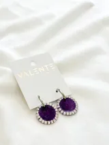 Par de aros colgantes con base circular de acrílico color violeta y borde con strass plateados. El aro es de acero plateado.