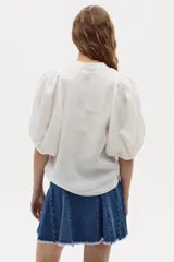 Camisa blanca de lino con cuello mao, cierre frontal con botones de nácar y mangas abullonadas hasta el codo.