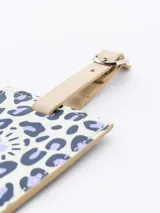 Identificador de maleta rectangular con estampado de manchas de leopardo color lila y corazones blancos. Correa de ajuste color beige con hebilla plateada.