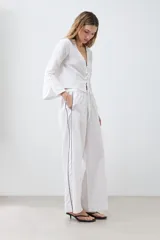 Pantalón de lino blanco de corte palazzo, con cintura elastizada y cordón ajustable. Presenta un vivo negro en el lateral.