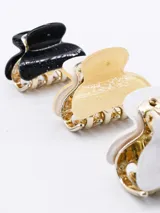 Set de tres pinzas para el pelo tipo clip, con cuerpo dorado y superficie en negro con glitter, amarillo con glitter y blanco con glitter.