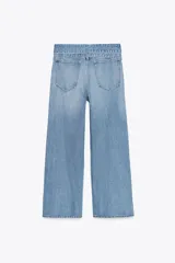 Pantalón de jean celeste de tiro alto, corte wide leg y largo hasta el tobillo. Incluye cinturón de la misma tela con trabillas y cierre frontal con cremallera, botón y gancho metálico.