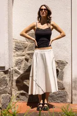 Falda midi evasé confeccionada en algodón de tono natural con contorno sutil en gris piedra que destaca las líneas de los recortes. La construcción por paneles aporta un vuelo ligero y una caída fluida, mientras que la cintura elastizada asegura un calce cómodo y limpio.