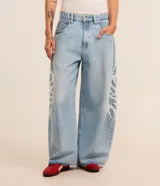 Pantalón de jeans celeste de corte amplio, con cintura con trabillas, cierre tradicional y bolsillos. Presenta estampa lateral estilo maorí en color blanco.