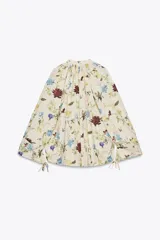Camisa color crema con estampado de flores en tonos azules, amarillos y borgoña. Tiene cuello redondo con escote en pico, mangas largas con lazos y bajo ajustable con cordones.