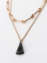 Collar doble dorado con cadena de eslabones grandes y cadena fina con dije colgante triangular negro.