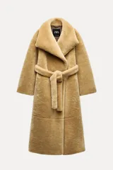 Abrigo largo color camel con efecto piel de oveja, cuello solapa, manga larga, bolsillos delanteros y cinturón ajustable con lazadas. Forro interior.
