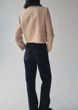 Chaqueta corta de tweed color rosa pálido con doble botonadura dorada, cuello redondo y bolsillos de parche en el pecho.