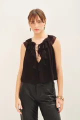 Blusa negra sin mangas, con escote en V profundo y volados en el frente. Tiene lazos en el cuello y gancho invisible para regular el escote.