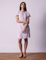 Vestido corto de lino a rayas verticales color lila y blanco, con cuello fruncido, escote en V y lazo de ajuste. Mangas cortas con puntilla de crochet.