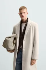 Abrigo straight fit color beige confeccionado en tejido con lana. Cuello con solapas de muesca, manga larga acabada en puño con botones, bolsillos de vivo en cadera, detalle de bolsillo interior y bajo con abertura en centro espalda. Cierre frontal de botonadura.