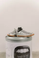 Zapatilla plateada de cuero con detalles de gamuza gris y costuras visibles.