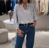 Blusa celeste y blanca a rayas verticales, de manga larga con puños abotonados, escote en pico con cuello ruffle y cierre delantero con botón.