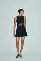 Vestido corto negro de cuello barco y sin mangas, con panel lateral de encaje floral transparente.