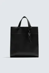 Bolso de hombro negro con compartimento principal con cierre mediante imán y bolsillo interior con cierre. Incluye charm colgante, dos asas de mano y un asa de hombro ajustable y extraíble.