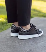 Zapatillas acordonadas de cuero color marrón con detalles dorados en el talón y suela blanca.