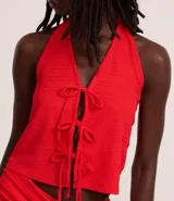 Vestido midi rojo, con textura plisada o arrugada, escote halter en V y detalle de amarras ajustables en el centro del busto que generan una abertura frontal. La falda presenta un fruncido lateral y una abertura alta.