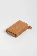 Billetera color tostado con diseño capitoneado en forma de V y tachas doradas. Cierre con cremallera y detalle de borla en el lateral.
