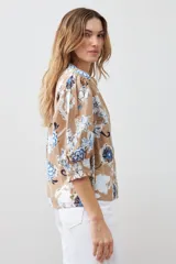 Camisa de manga 3/4 abullonada con puño elastizado, cuello mao y estampado floral en tonos azules y blancos sobre fondo tostado.