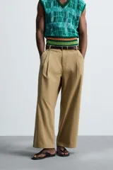 Pantalón color beige de corte ancho, con pliegues frontales dobles, bolsillos laterales y traseros de vivo. Largo cropped y cierre frontal con cremallera y botón.