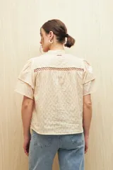 Camisa blanca de algodón liviano con diseño calado, cuello mao, mangas cortas abullonadas y detalle de pasamanería en el frente.